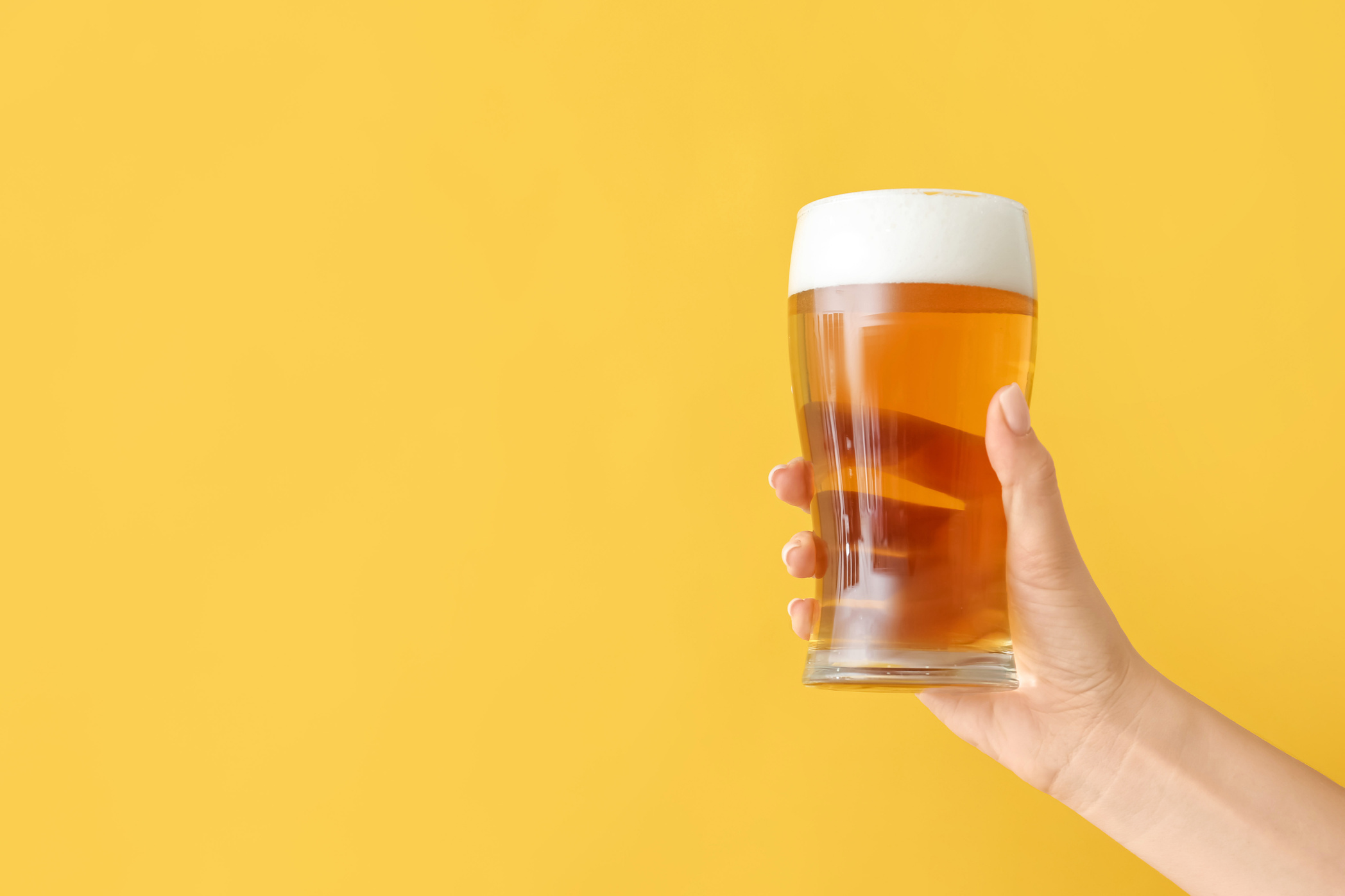 Hand with Glass of Beer on Yellow Background